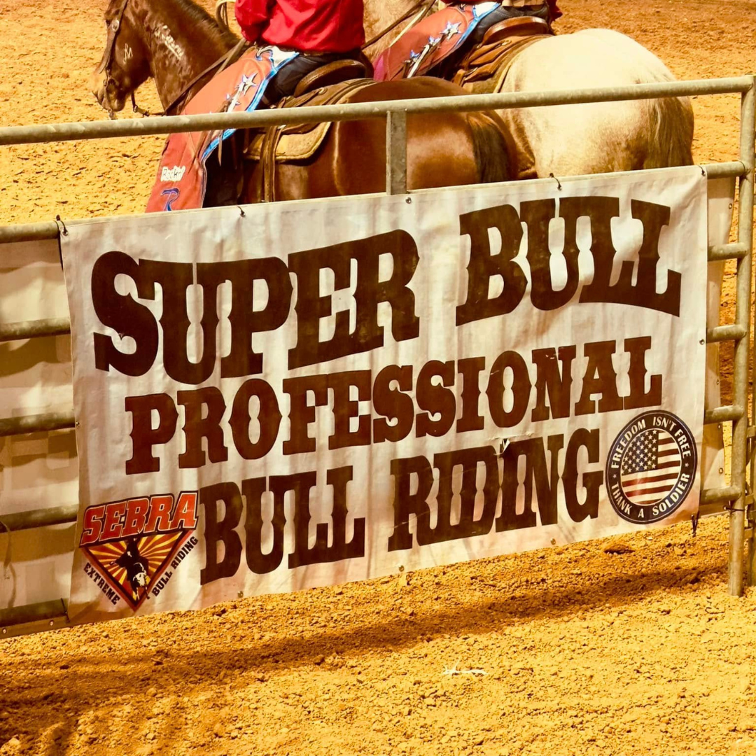 banner hanging on the side of a corral for a bull riding competition