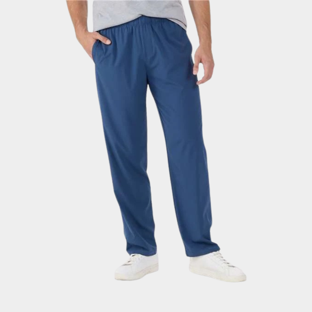 bottom half view of man wearing a grey shirt, blue sweatpants and white shoes. Posed with one hand in pocket.