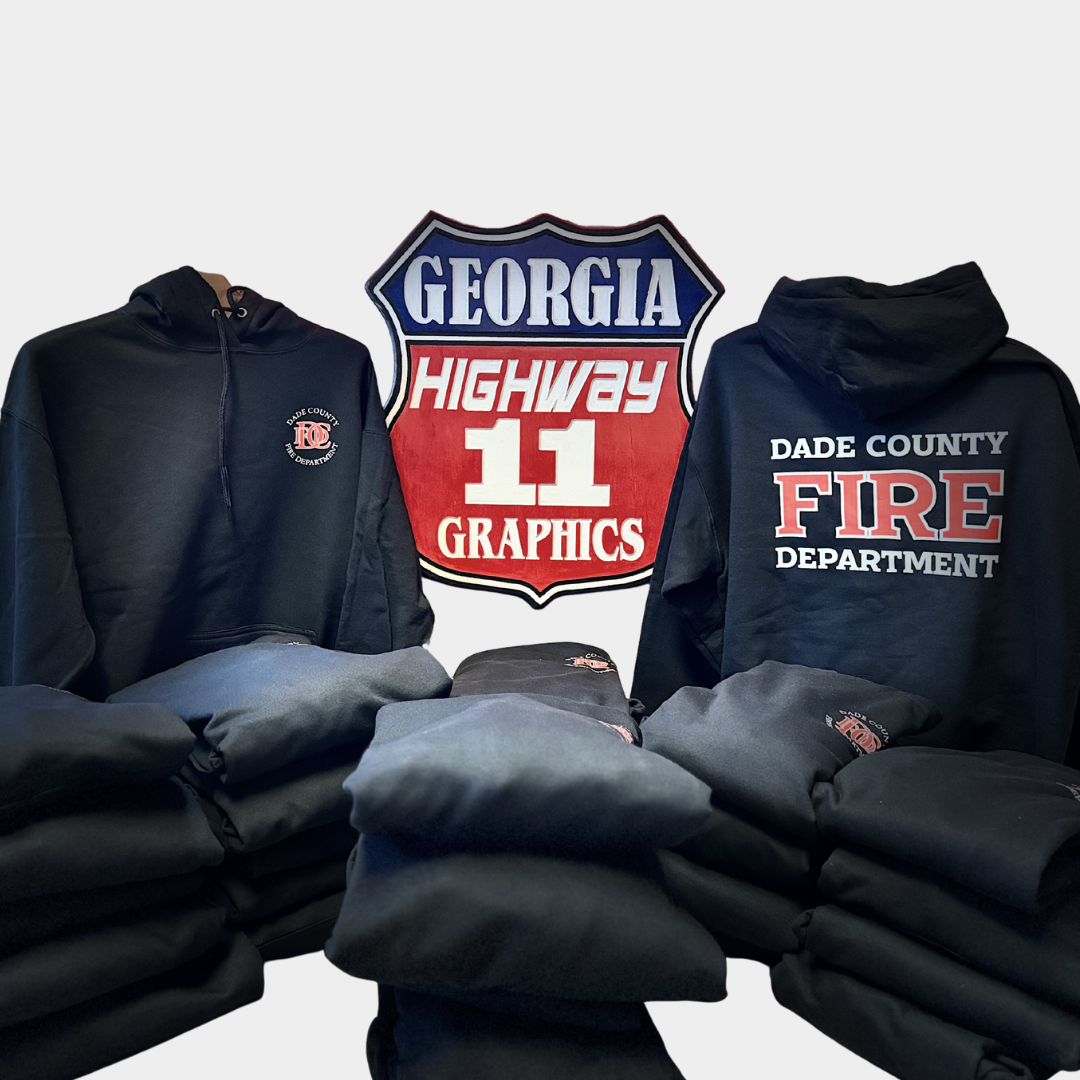 two hoodies in between Highway 11 Graphics logo with a pile of folded hoodies stacked below. All hoodies are black and say "Dade County Fire Department" in red and white lettering